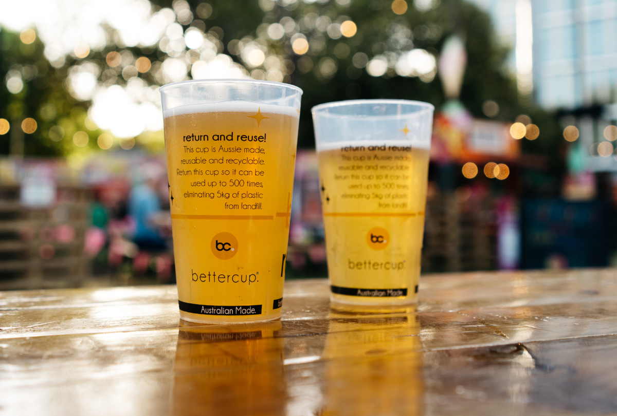 Reusable bettercup tumblers with beer on a wooden table at an outdoor event.
