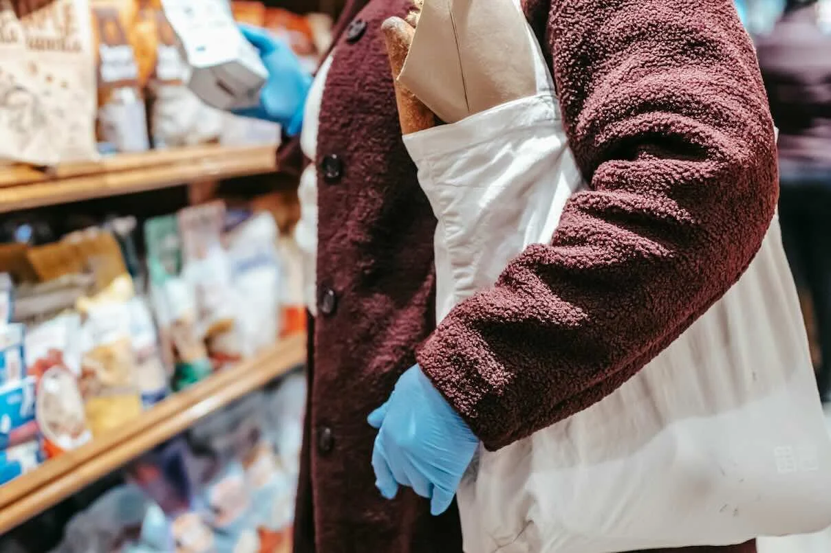 Shopper in supermarket with reusable shopping bag and gloves