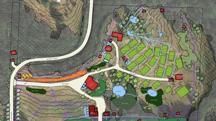 A detailed topographical map depicting a planned community layout with roads, buildings, green spaces, and water features. Various structures are labeled, and areas are color-coded to represent different zones or land uses. Topographical lines indica