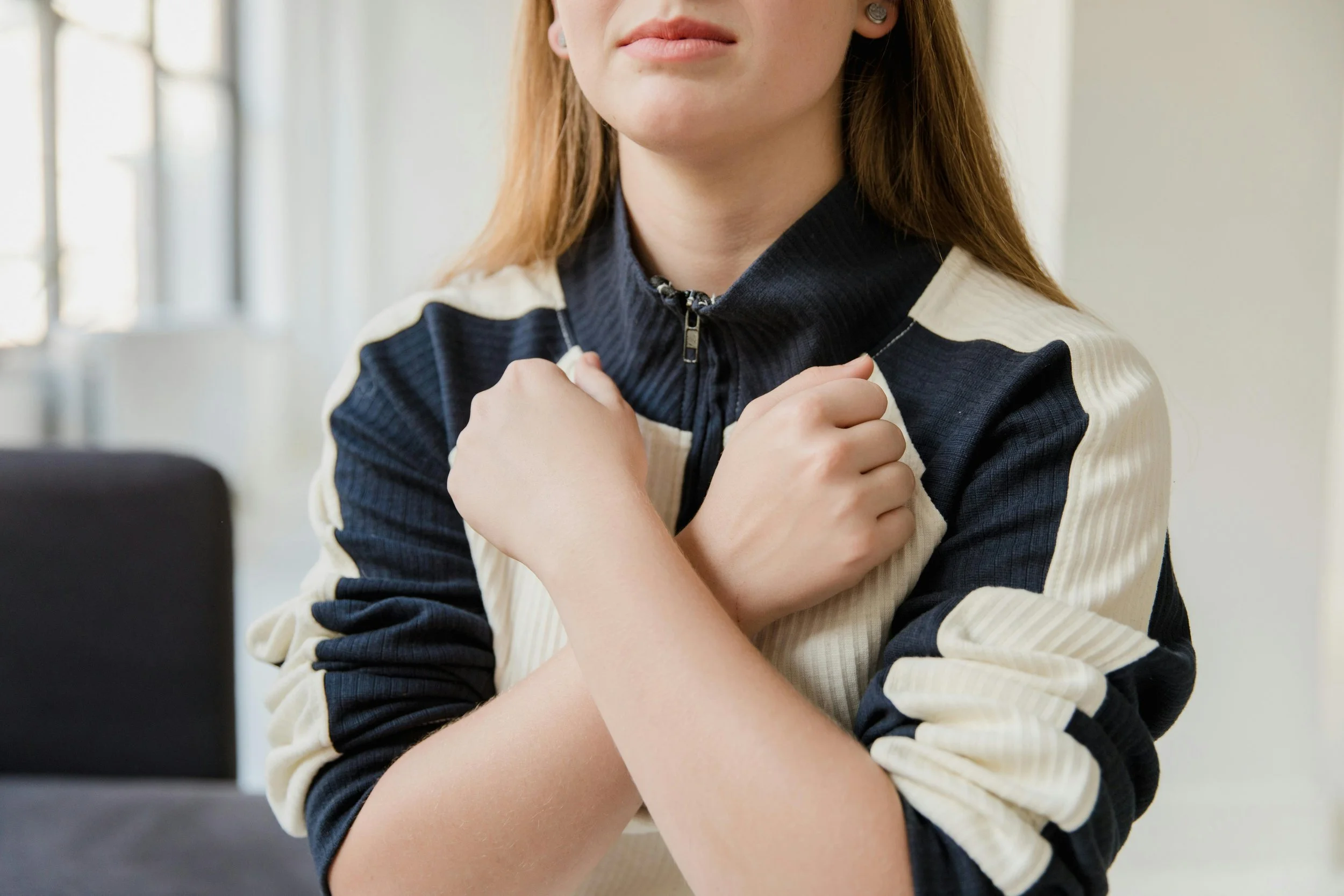 A close-up of a woman's hand resting gently on her shoulder, practicing a somatic reclamation and tapping exercise to connect with her body.