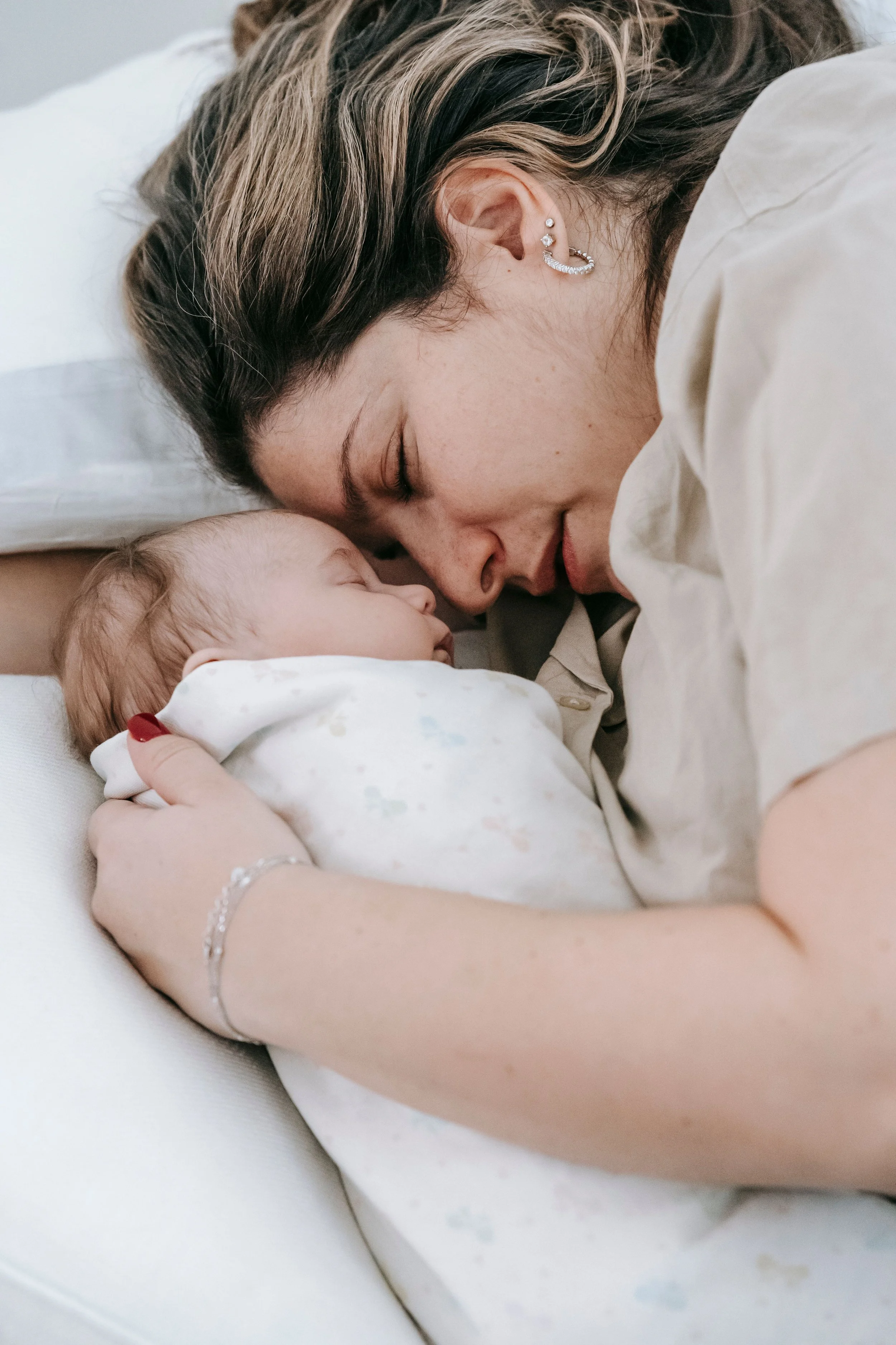 A mother tenderly holding her sleeping newborn baby against her chest in a dimly lit bedroom during a quiet night