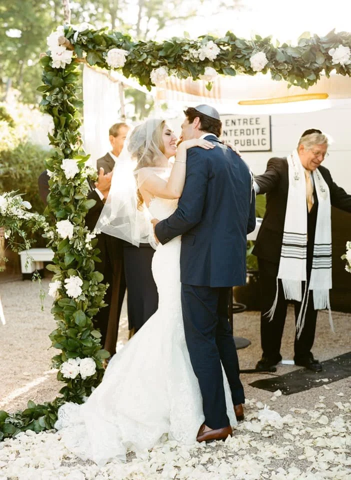 Bride and groom sharing a kiss under a floral arch during their outdoor wedding ceremony