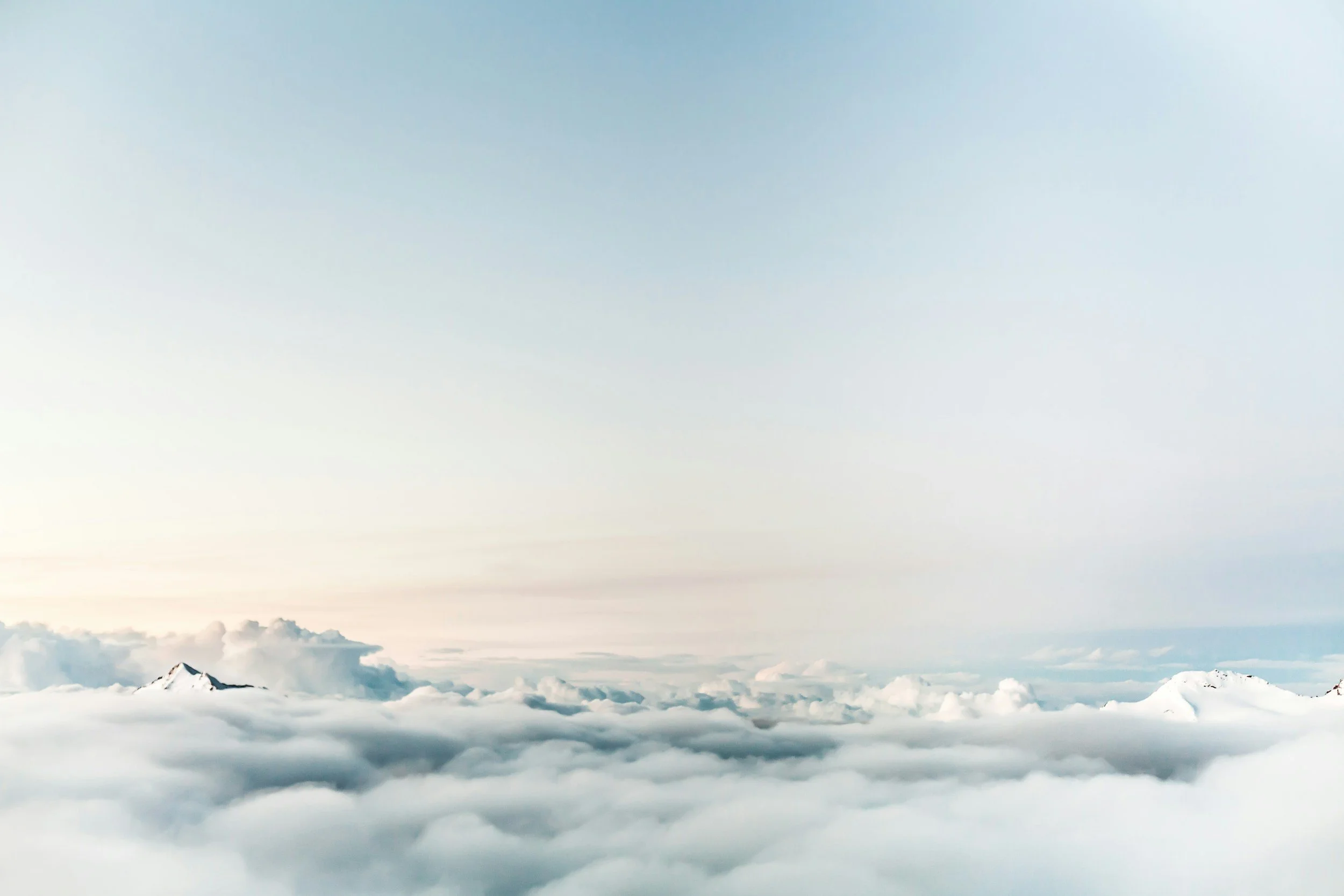 View of clouds from above with a mountain peak visible through the clouds.