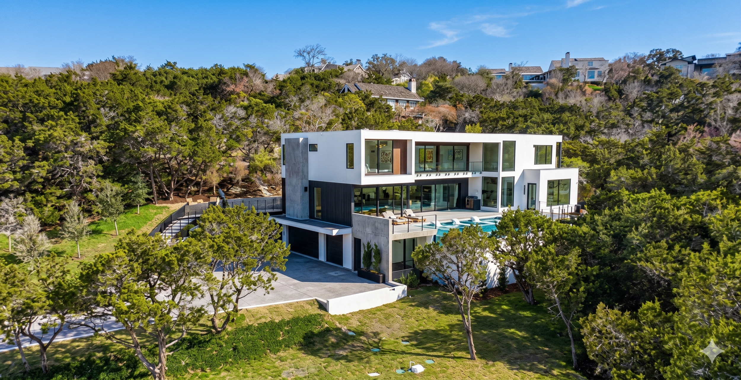 actual image of cedar oak residence in texas. Luxury residence built on a hillside, showing the infinity pool, driveway, stairs leading up to the second floor of the house. With blue skies, trees and other houses as a backdrop.