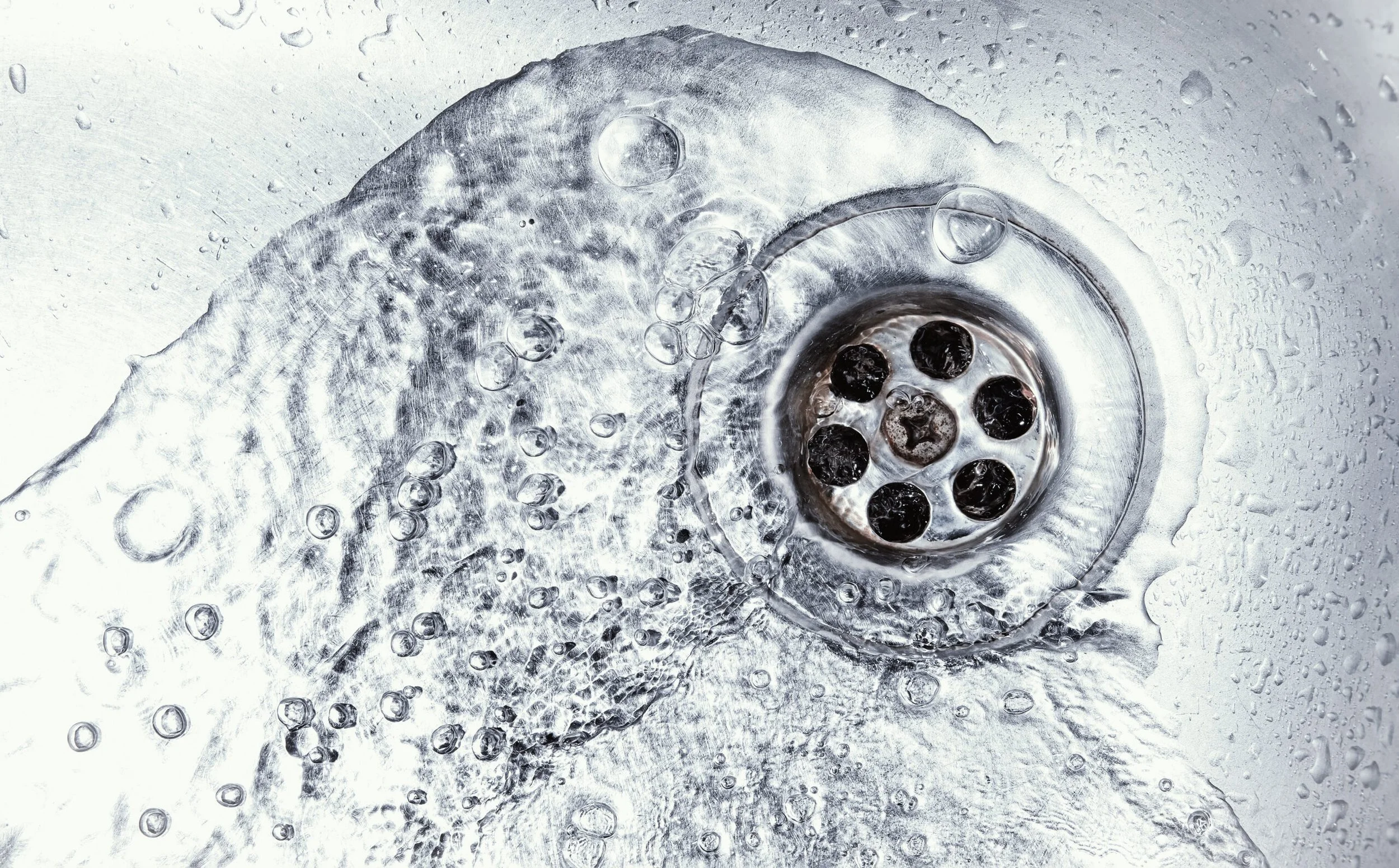 Close-up view of a sink drain with bubbles and water around it.