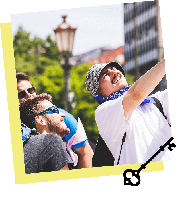 A group of friends taking a selfie outdoors during daytime, with a historic streetlamp and green trees in the background, smiling and enjoying the moment.