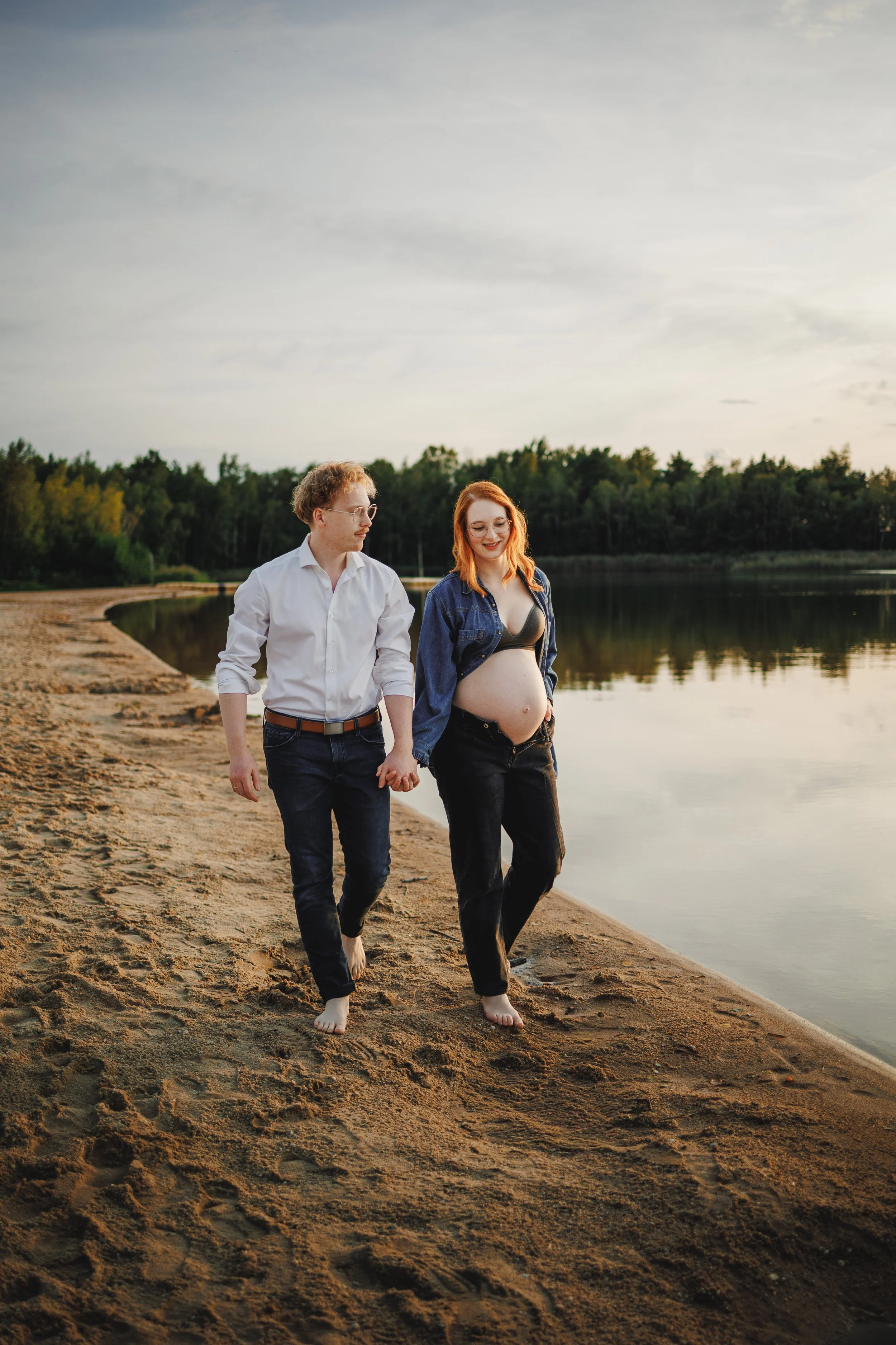 Babybauchshooting am Wasser bei weichem Abendlicht: Ein werdendes Paar läuft barfuß am Strand entlang, hält Händchen und genießt den Moment – ruhig, natürlich und ungestellt. Genau solche authentischen Babybauchfotos entstehen, wenn wir uns bewegen, 