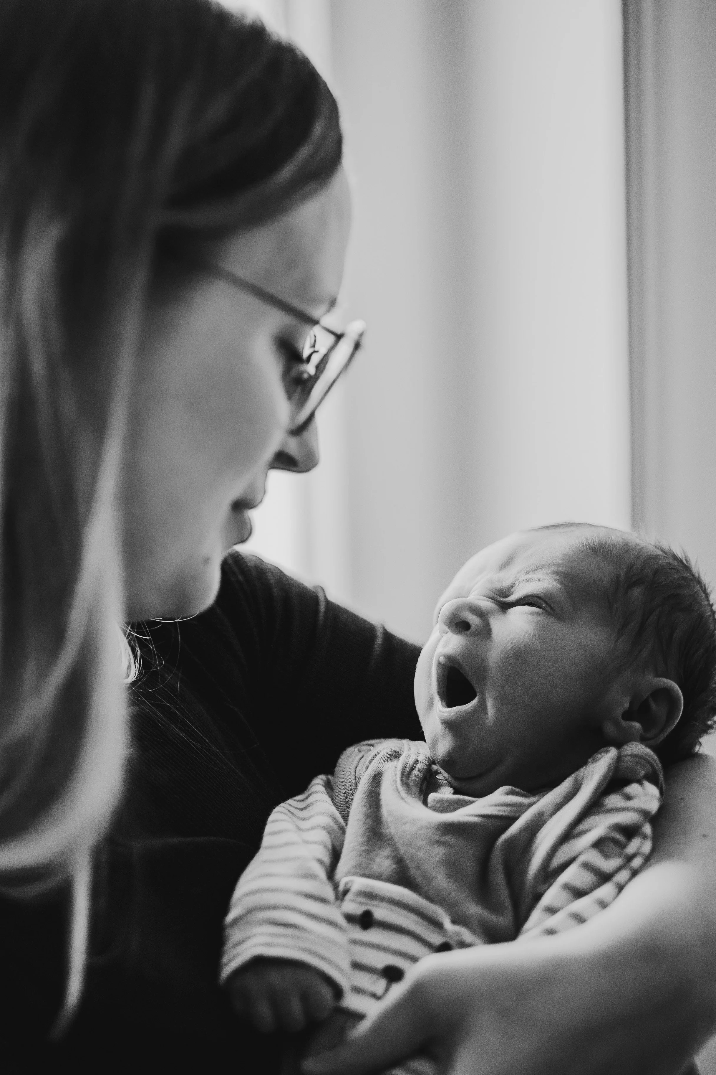 Authentischer Moment aus einem Newbornshooting zuhause: Mama hält ihr Neugeborenes im weichen Fensterlicht – ruhig, nah und zeitlos in Schwarzweiß.