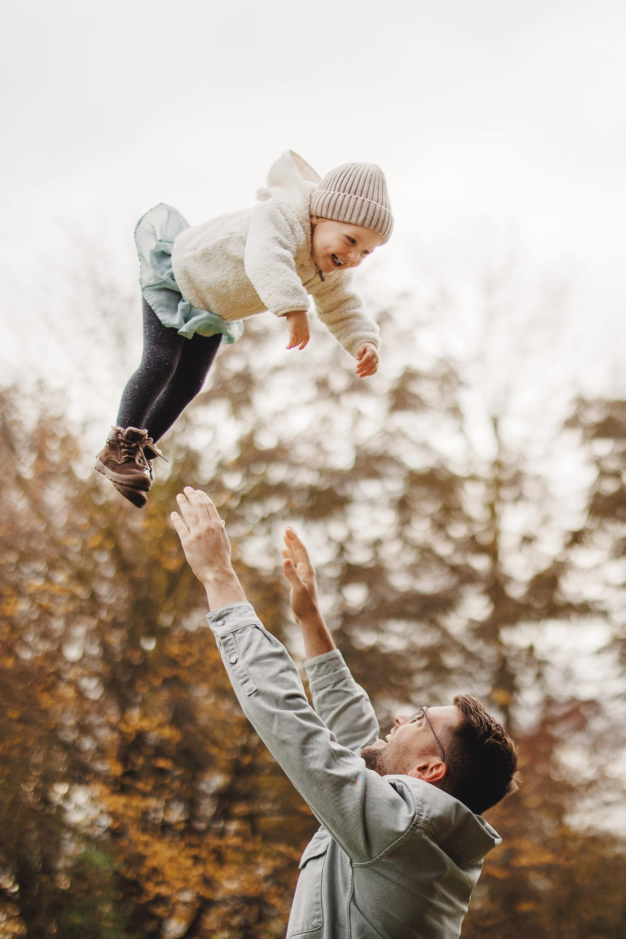Echter Familienmoment in Bewegung: Papa wirft sein Kind in die Luft – viel Lachen, Nähe und Herbststimmung. Natürliches Licht, ungestellt und lebendig.