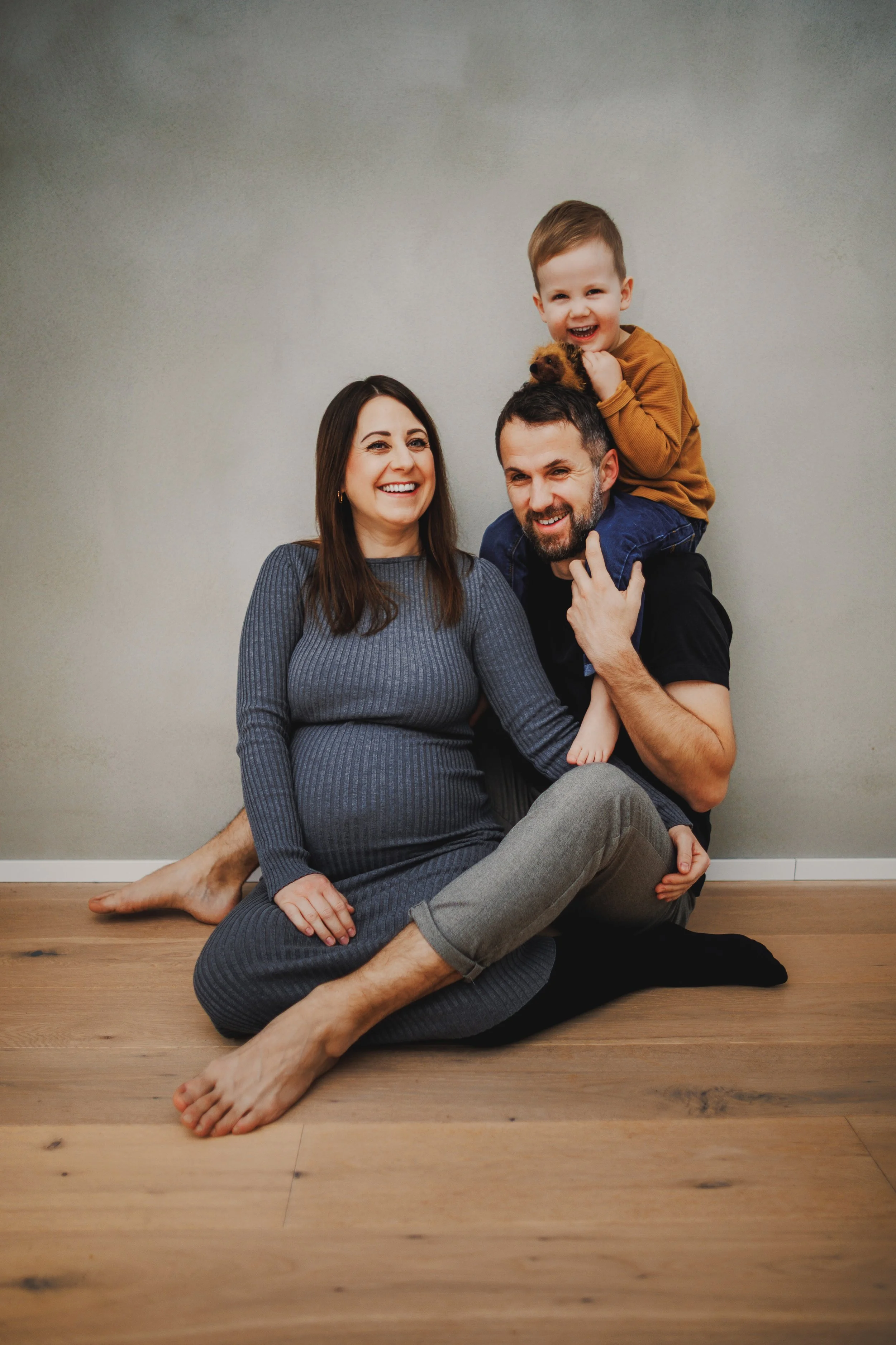 Babybauchshooting in entspannter Home-Atmosphäre: Die werdenden Eltern sitzen gemeinsam mit ihrem Kind auf dem Boden – nah, locker und ohne steife Posen. Genau solche Familienmomente fotografiere ich am liebsten: echt, warm und unaufgeregt, mit Fokus