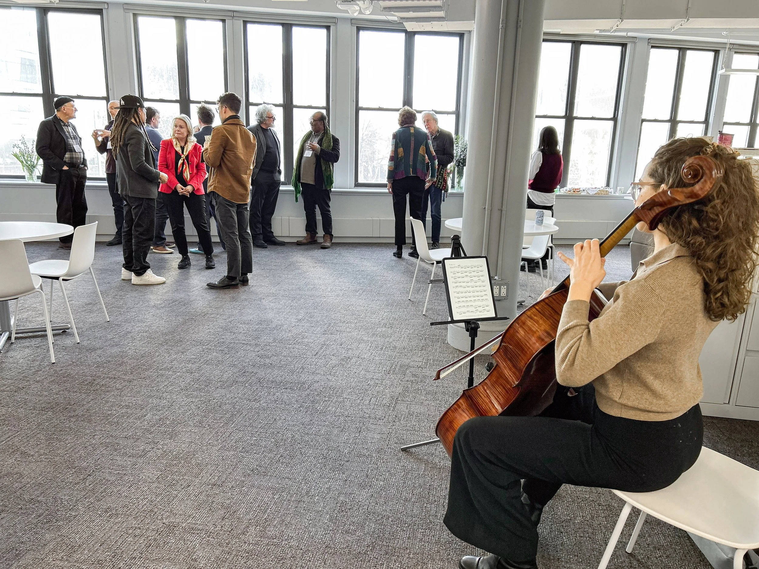 A cellist performing as participants talk during a break at a COMIT gathering
