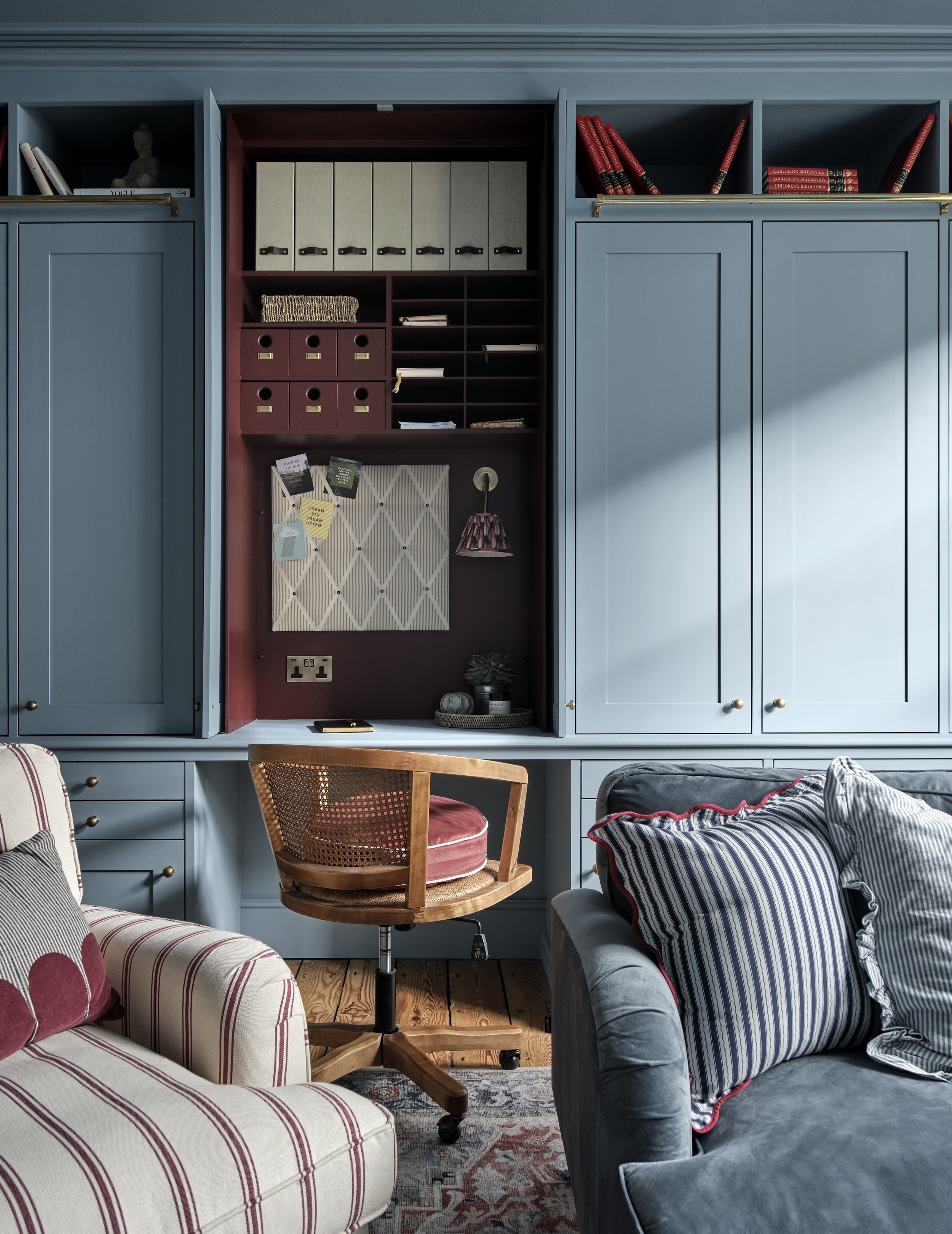 Living room with built-in blue cabinets, a wooden swivel chair with a pink cushion, striped pillows on a gray sofa, and a patterned rug.