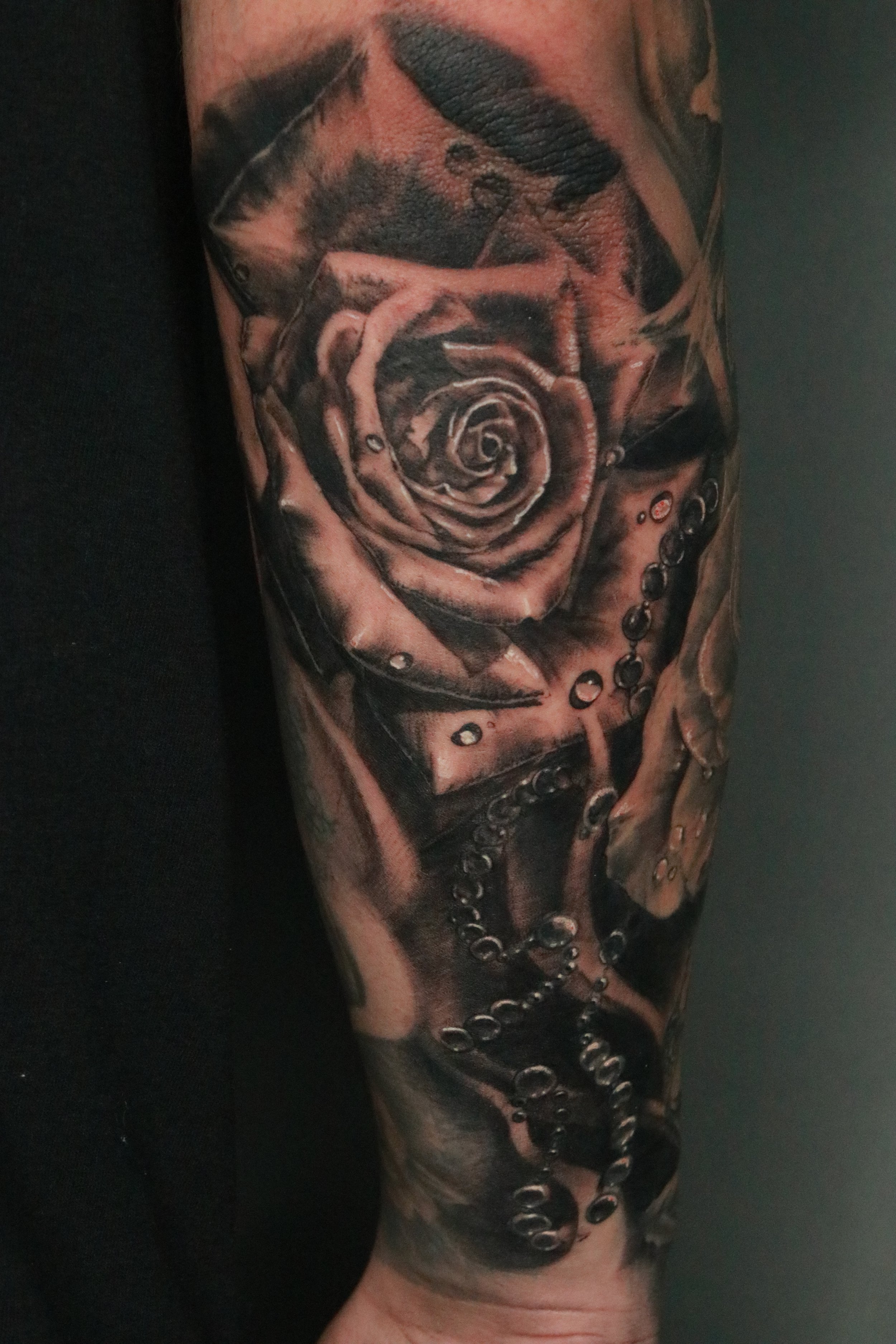 Black and gray realistic tattoo of a rose and a pocket watch on a person's arm, with water droplets and chain details. Custom Tattoos available at Molina's Art Tattoo Studio in Toronto.