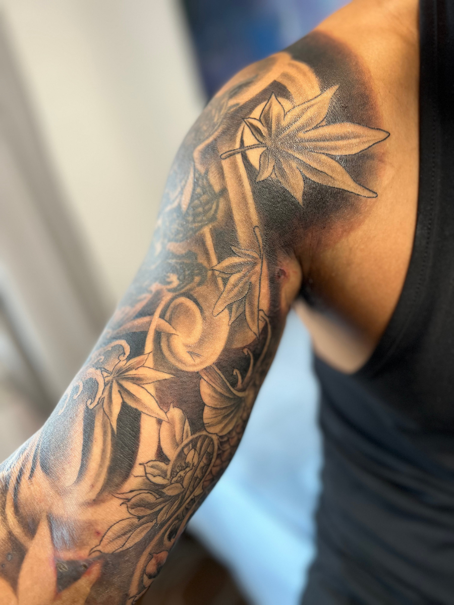 Close-up of a person's upper arm tattoo featuring a woman's face surrounded by leaves and floral elements in black and gray shading. Custom Tattoos available at Molina's Art Tattoo Studio in Toronto.