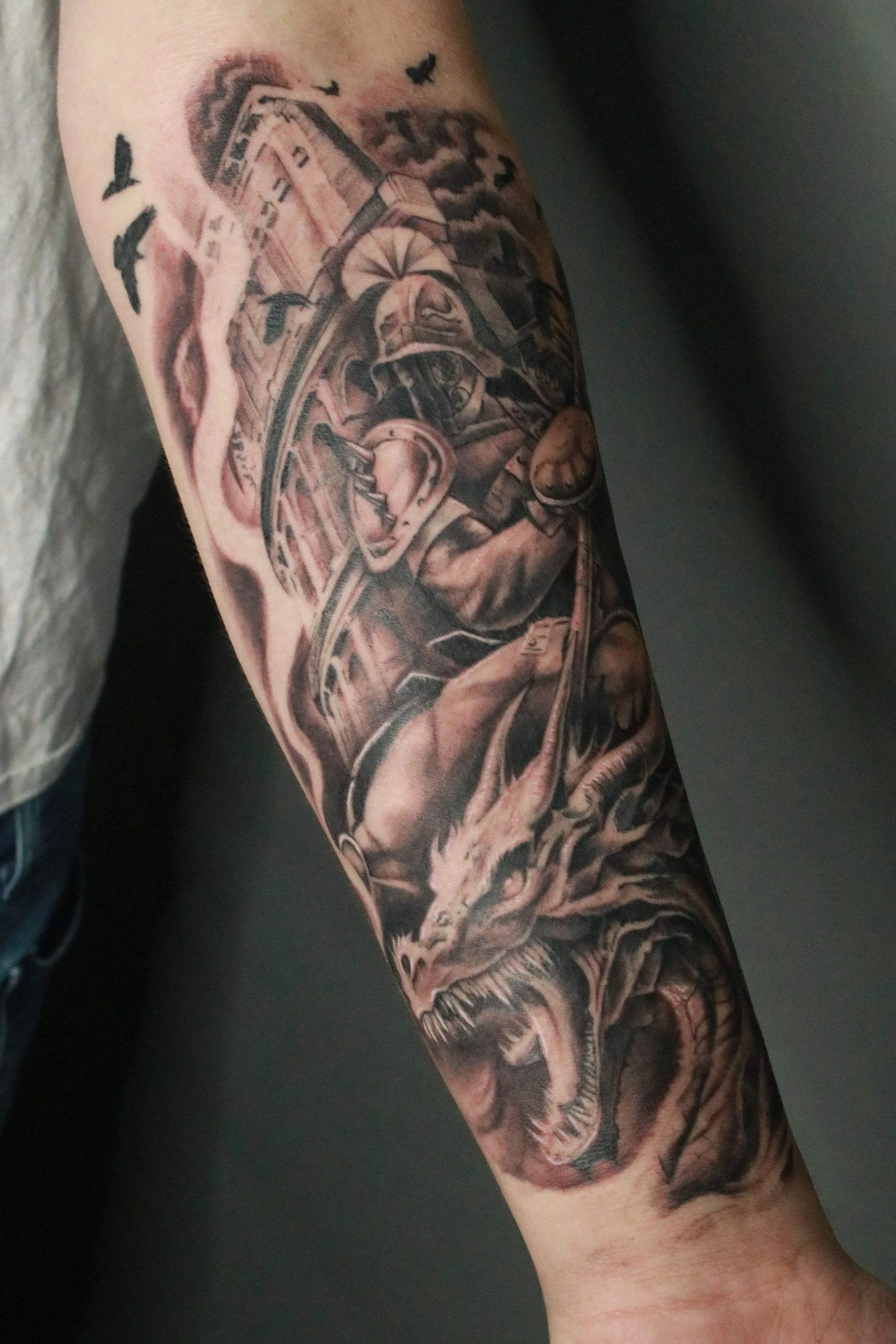 Black and gray tattoo featuring a fierce dragon and a detailed scene with a building and bats. Custom Tattoos available at Molina's Art Tattoo Studio in Toronto.