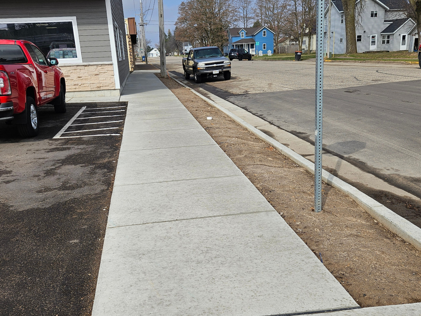 Worn sidewalk next to a parking lot with bare soil