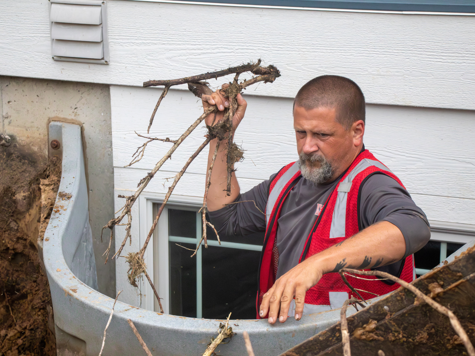  Crew member removing soil and roots from window well area 