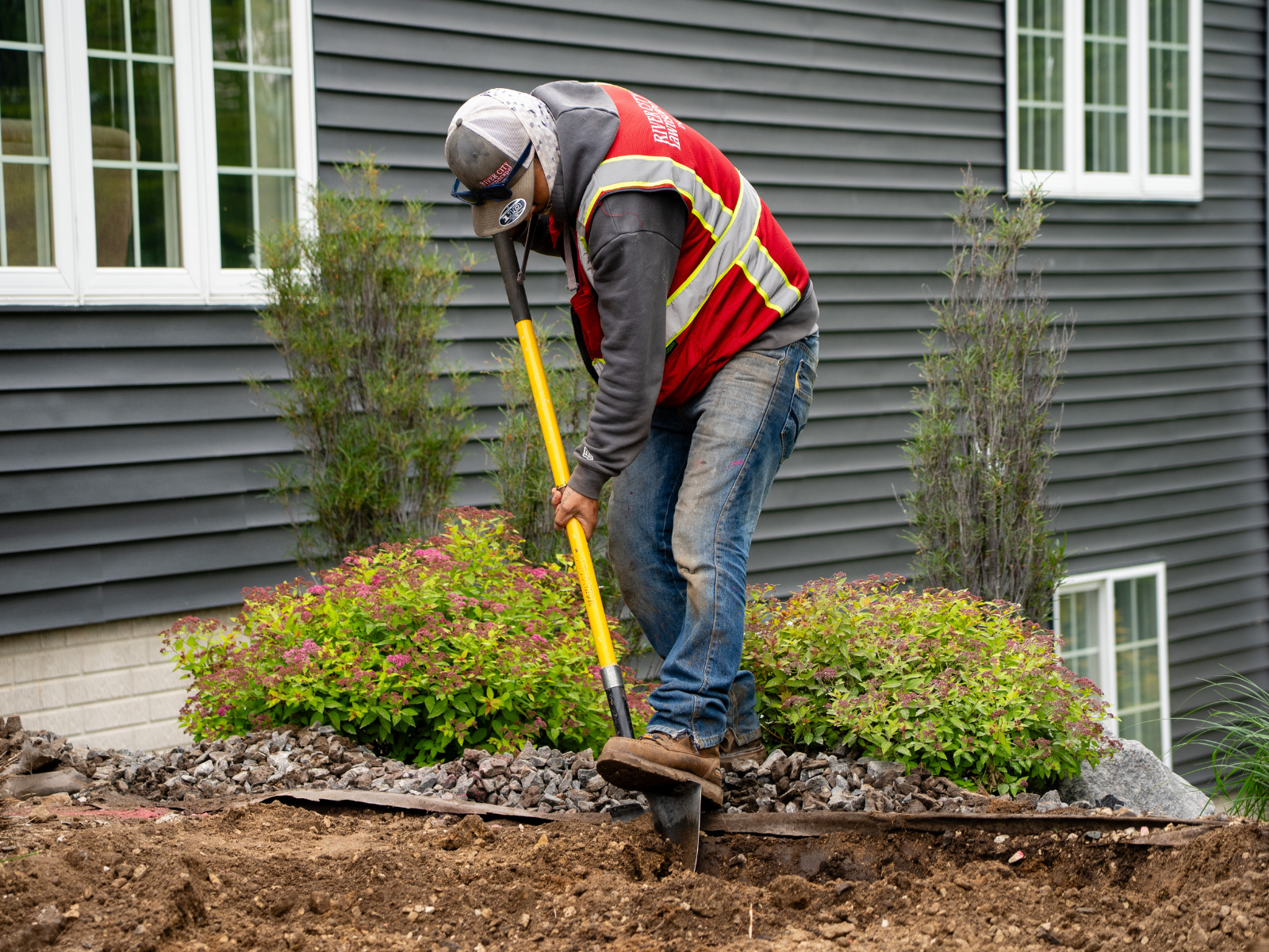 Crew member preparing landscape bed near the home during site work.