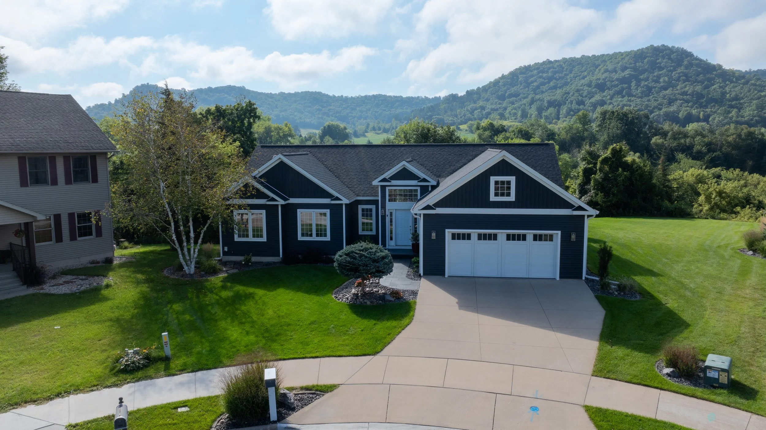 Wide aerial view of completed home exterior and surrounding landscape.
