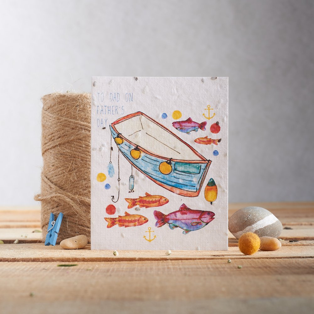  Seed embedded greeting card in nautical design photographed with pebbles and twine on rustic planked surface 