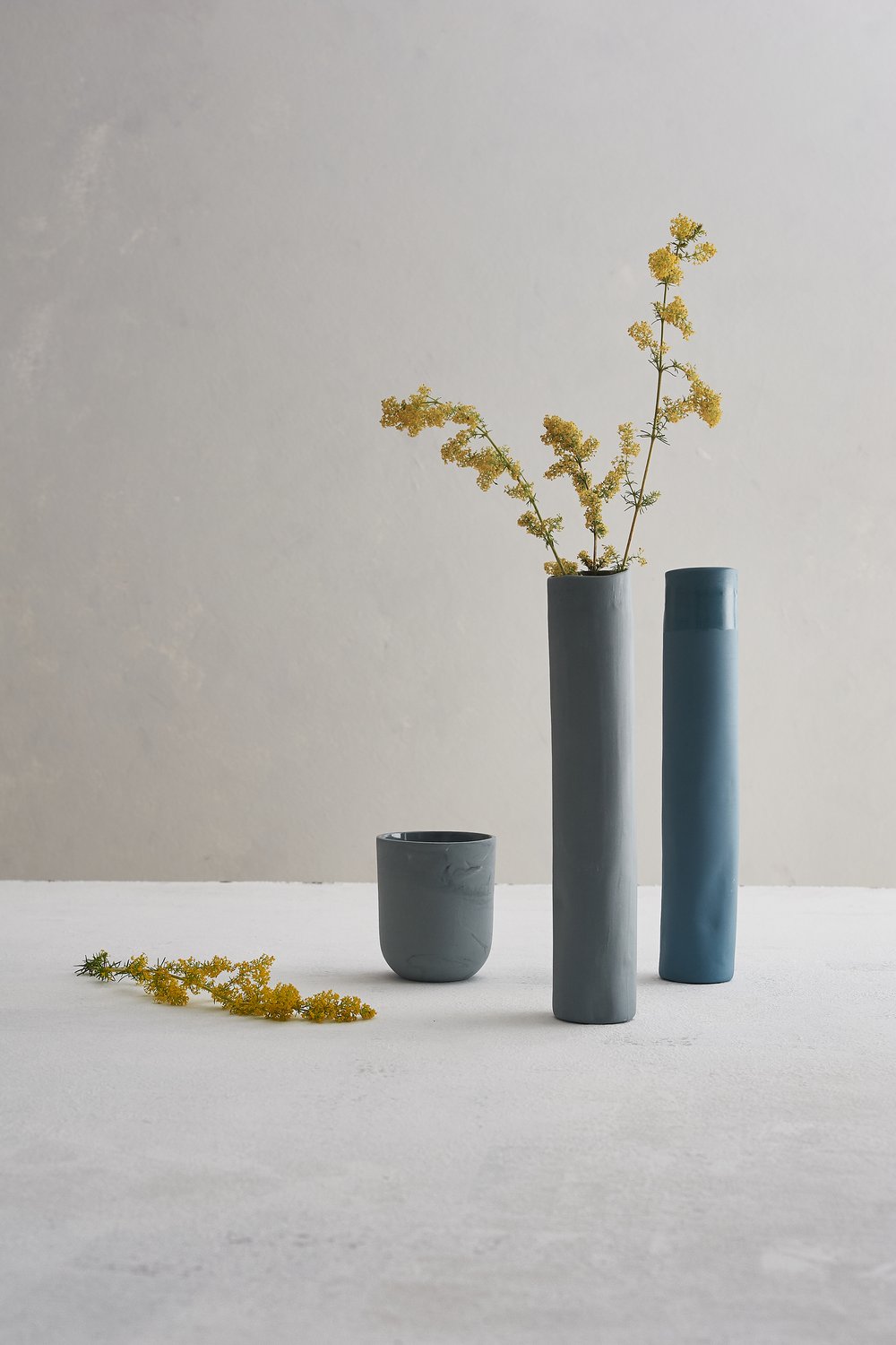  Still life image of handmade ceramic vases and beaker photographed on hand lightly textured and painted surface and background 