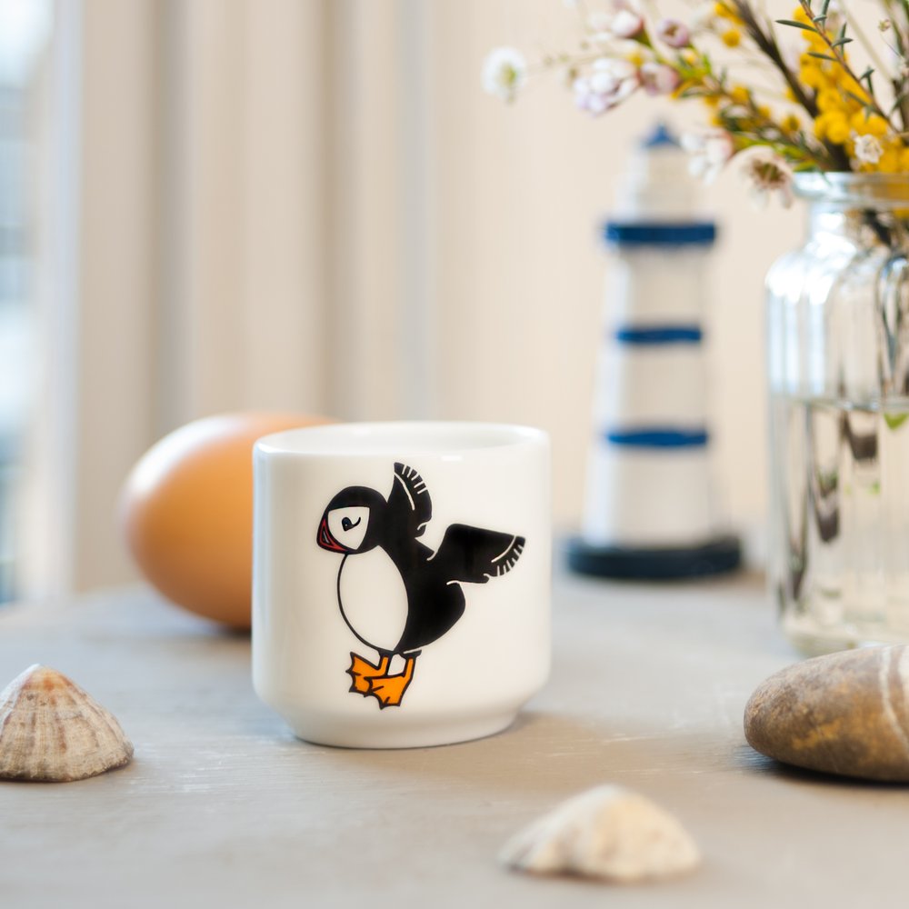  Puffin illustrated small beaker on table, window in background to the side, props including egg and coastal props 