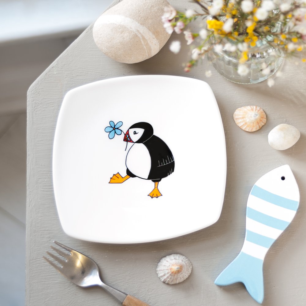  Puffin illustrated plate on table, props including  coastal props like pebbles 