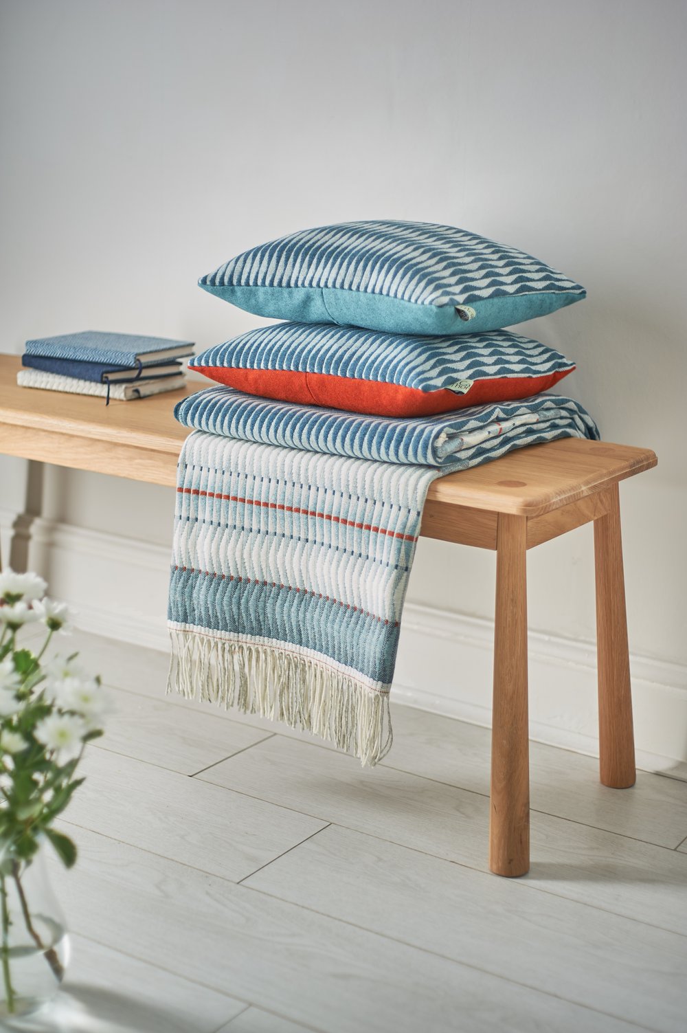  Handmade designer textiles throws cushions stacked up on top of wooden bench 
