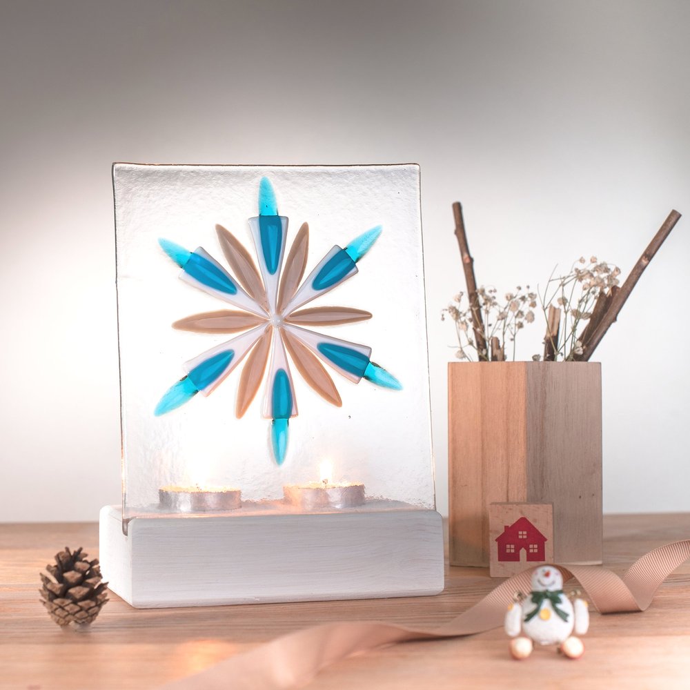  Decorative glass tea light holder with geometric design to front surrounded with Christmas props including pine cone and twigs 