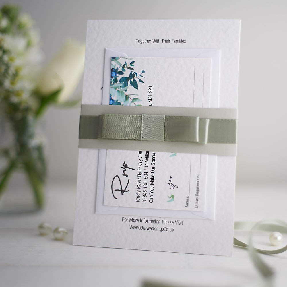  Wedding stationery photographed next to fresh flower in small glass vase out of focus in background 
