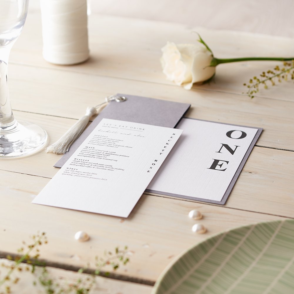  Mock-up of wedding stationery diagonally strewn across table with fresh flowers and champagne flute as props 