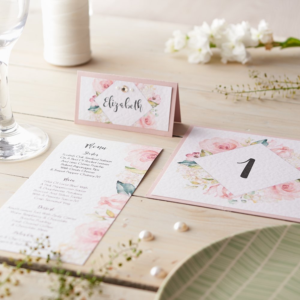  Mock-up of wedding stationery diagonally strewn across table with fresh flowers and champagne flute as props 3 