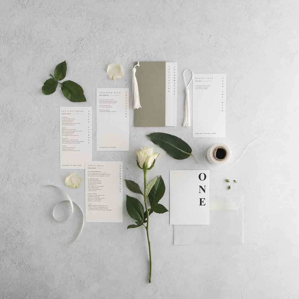  Flat-lat of complete wedding stationery suite layered with surrounding props including leaves and fresh flowers photographed upon concrete background 2 