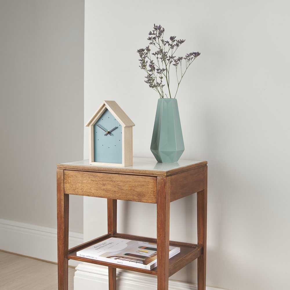  Small mid century table with handmade wooden clock on top in shape of a house next to a vase 