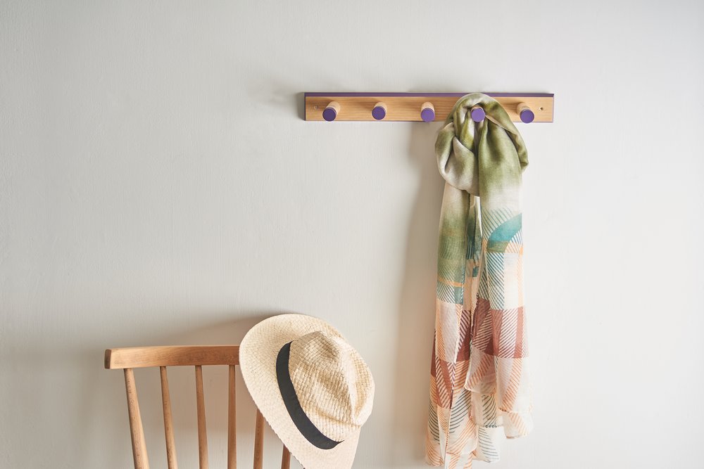  Photograph of handmade wooden coat hanger with throw hung, next to chair with hat 