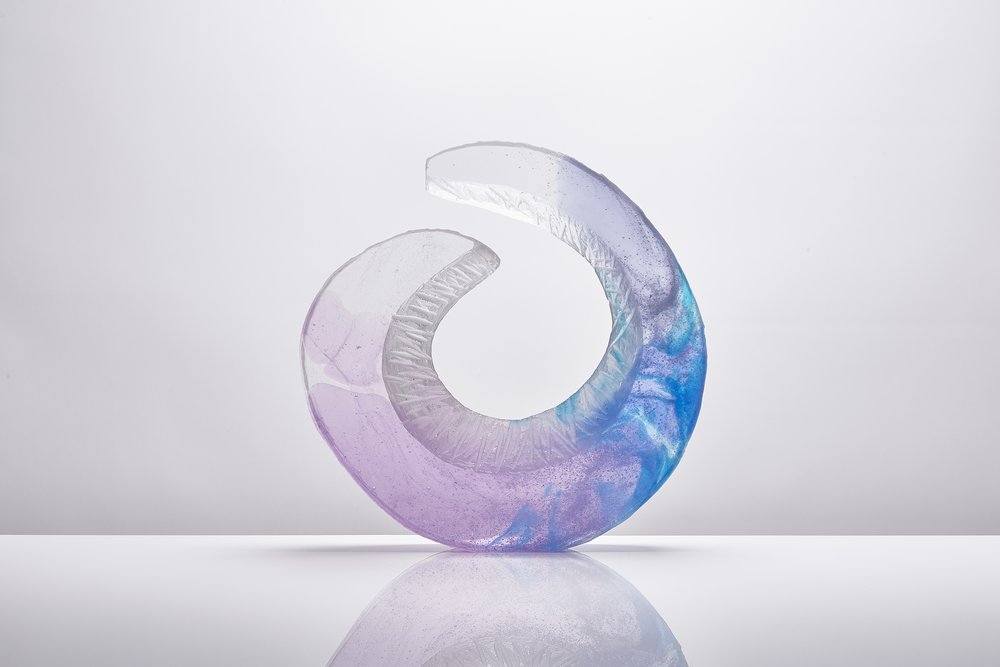  Curved sculptural piece of glass with intricate detailing within photographed on glossy white surface with reflection 