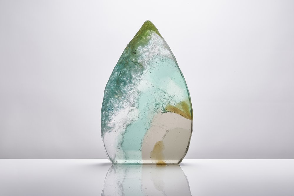  Sculptural piece of glass in green with intricate detailing within photographed on glossy white surface with reflection 
