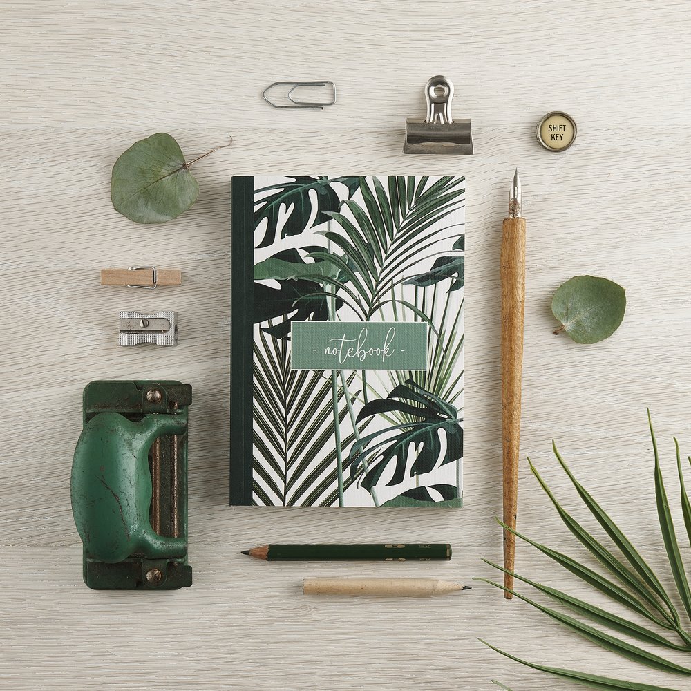  Designers notebook photographed with colour coded green stationery props and palm leaf 