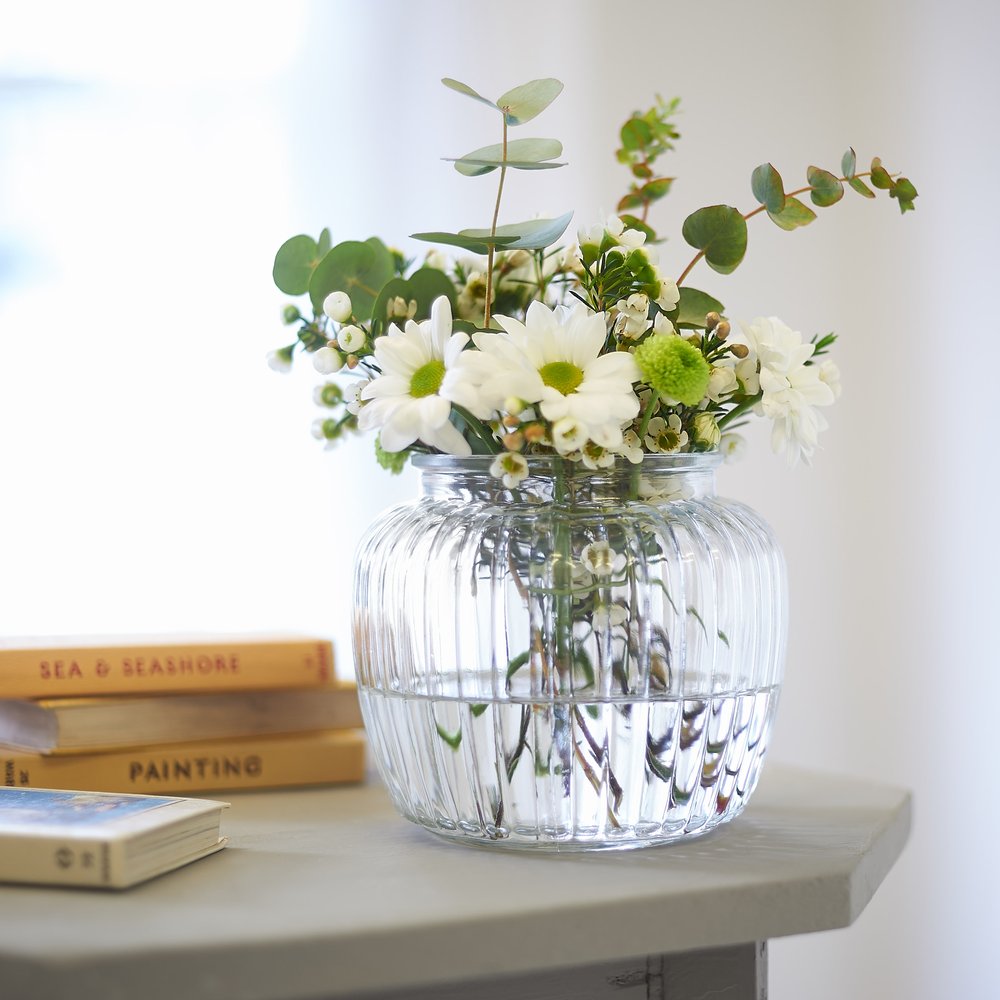  Faux eucalyptus and other stems in ribbed glass vase with light from window behind and vintage books 