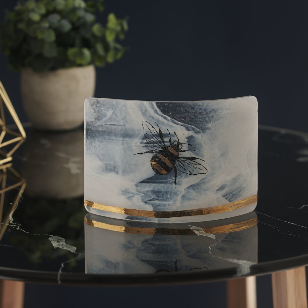 Glass decorative tealight holder with bee design upon, photographed on black glass side table and plant as prop 