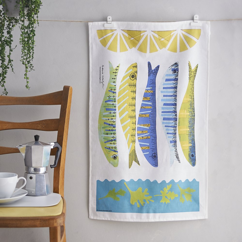  Designer illustrated teatowel photographed upon washing line against pale grey backdrop and kitchen chair 