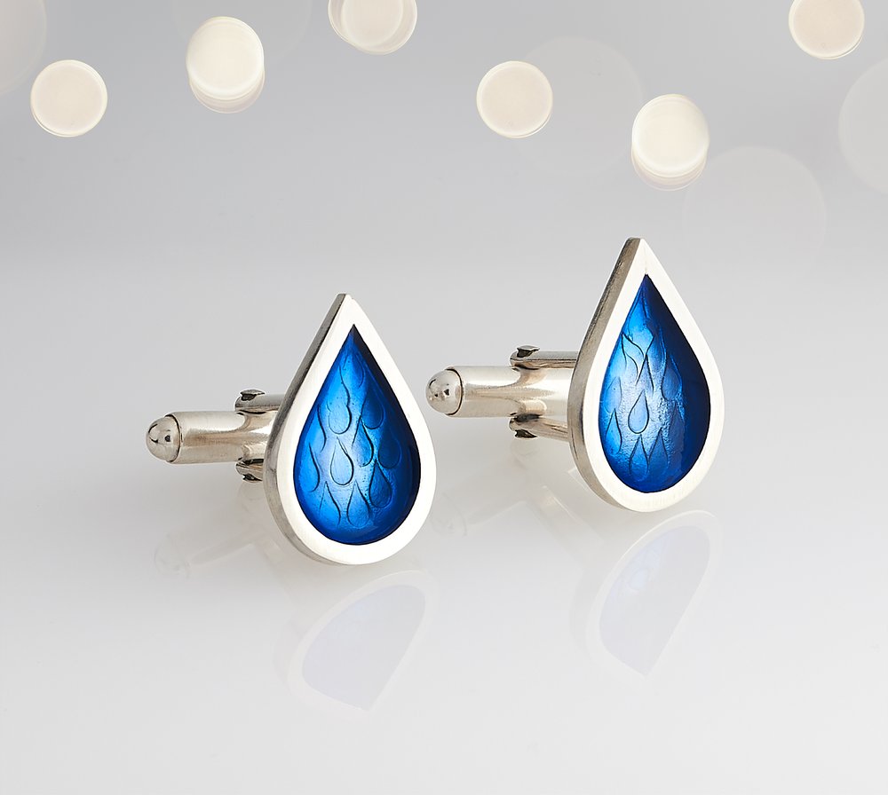  Rain drop shaped vivid blue and silver cufflinks photographed with out of focus bright lights in background 