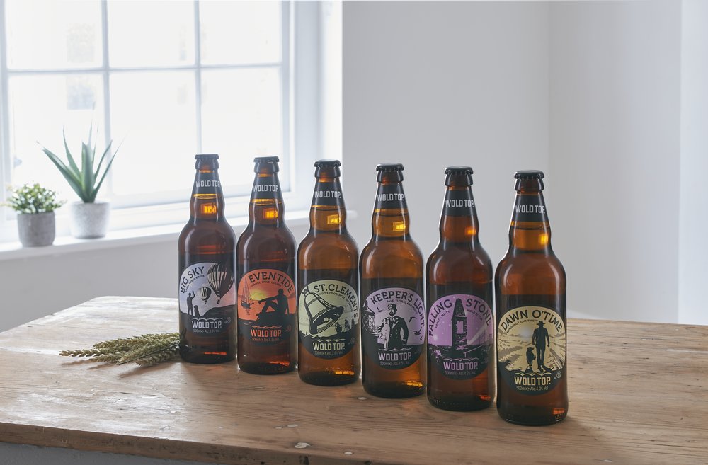  A line up of six beer bottles photographed in a photography studio with window  to the side 