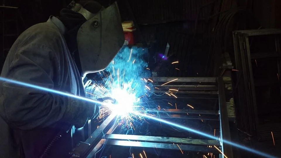 The mastery of iron and welding projects in our gallery as our skilled professional works diligently in our warehouse. He is dressed with his  protective uniform, mask, and gloves.