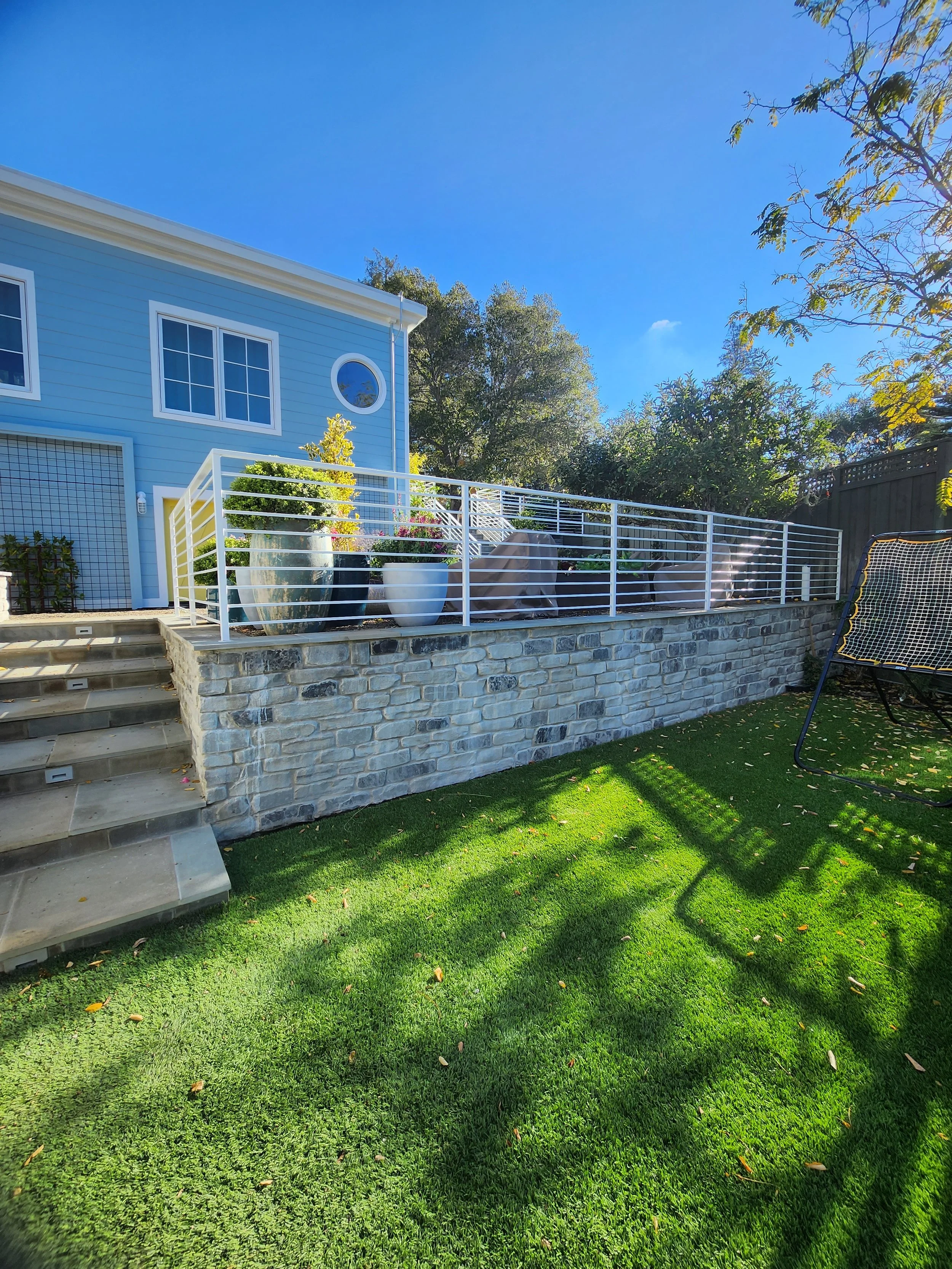 Small white rectangular fence next to the stairs and the fence separating the green area from the house.