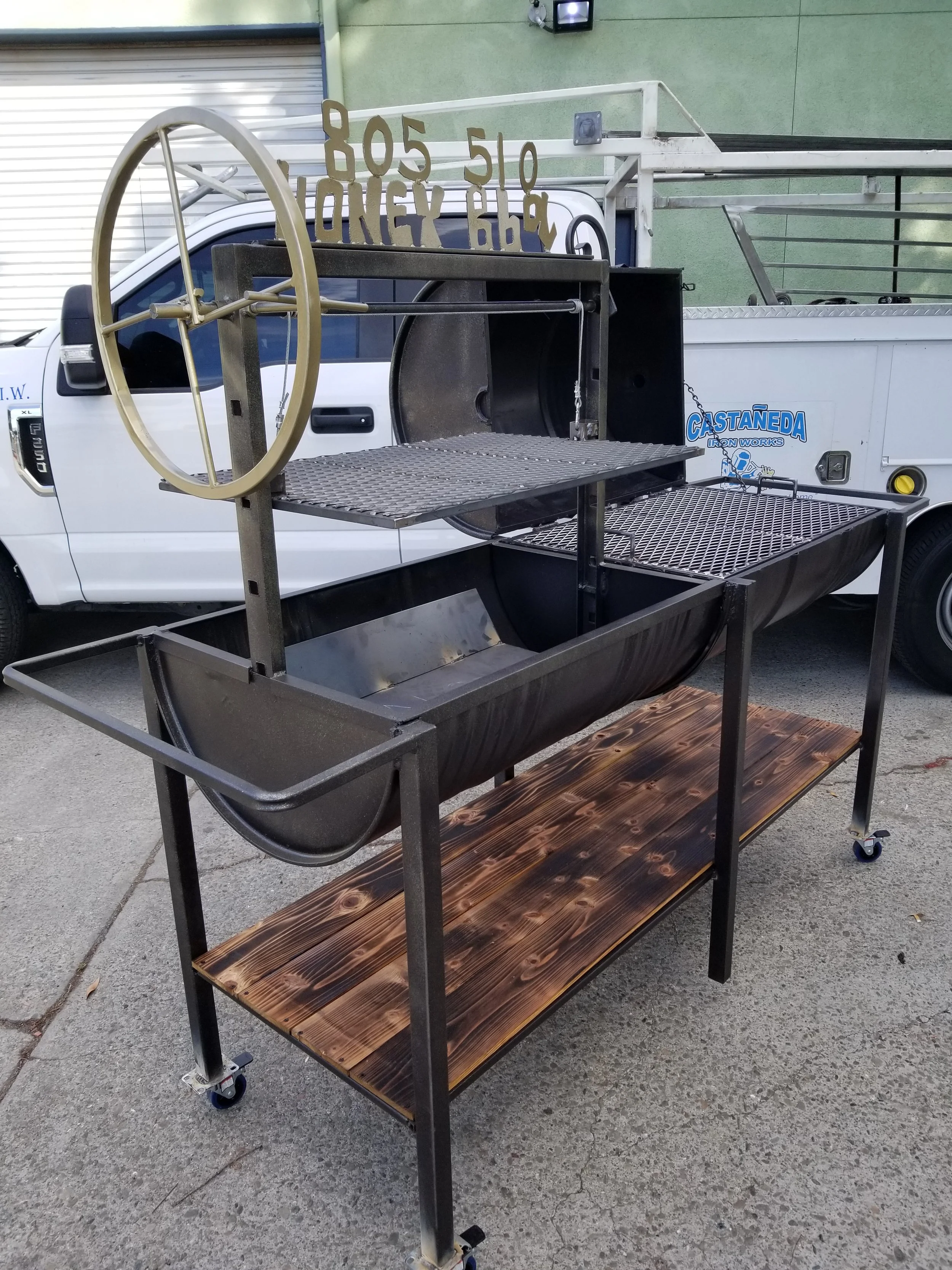 The black bbq pit with the grills made in iron by the welding professional and a wooden base to place the utensils needed.