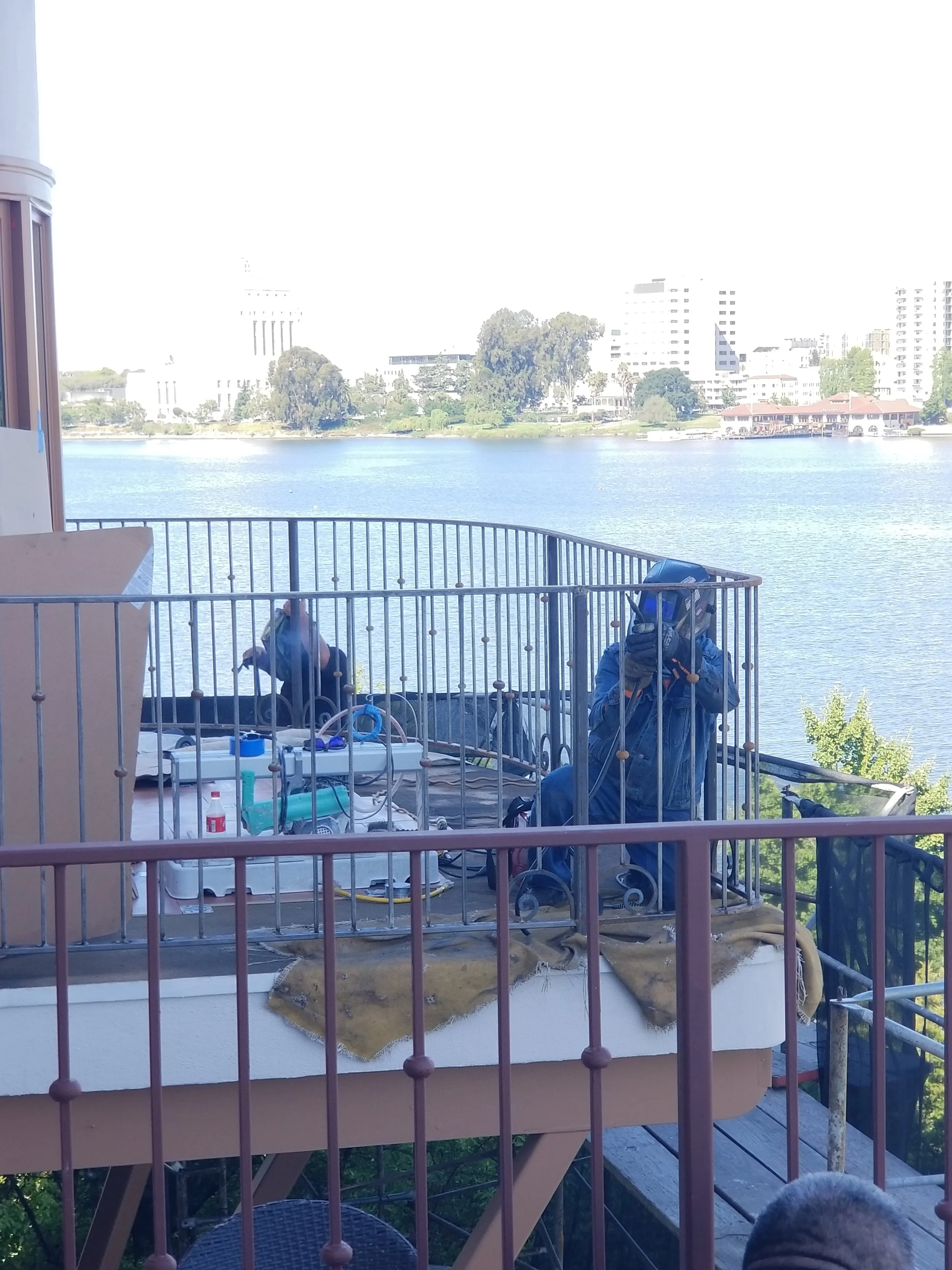 The iron welding team is working on a apartment balcony  with a like as a view.
