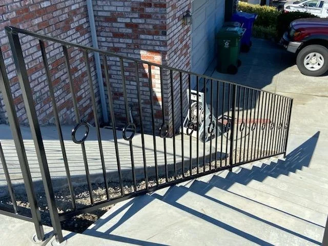 A black rectangular fence for the main entrance of a house with circular details for the separation of stairs.