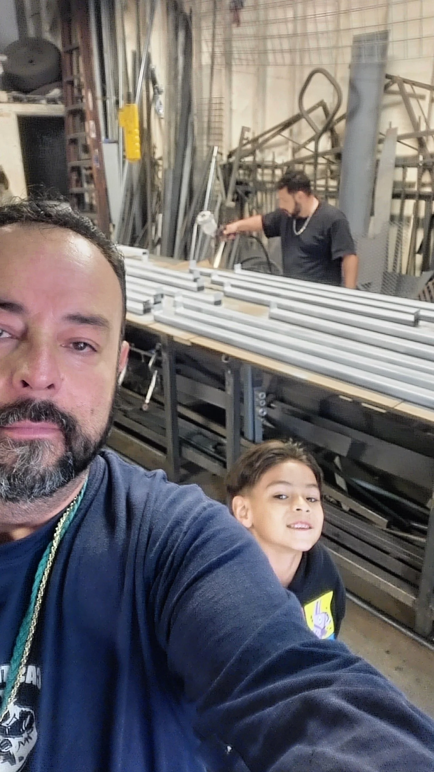 The expert in welding iron takes a selfie with a young enthusiast. Behind them stand iconic white columns, showcasing the blend of craftsmanship and joy in our projects.