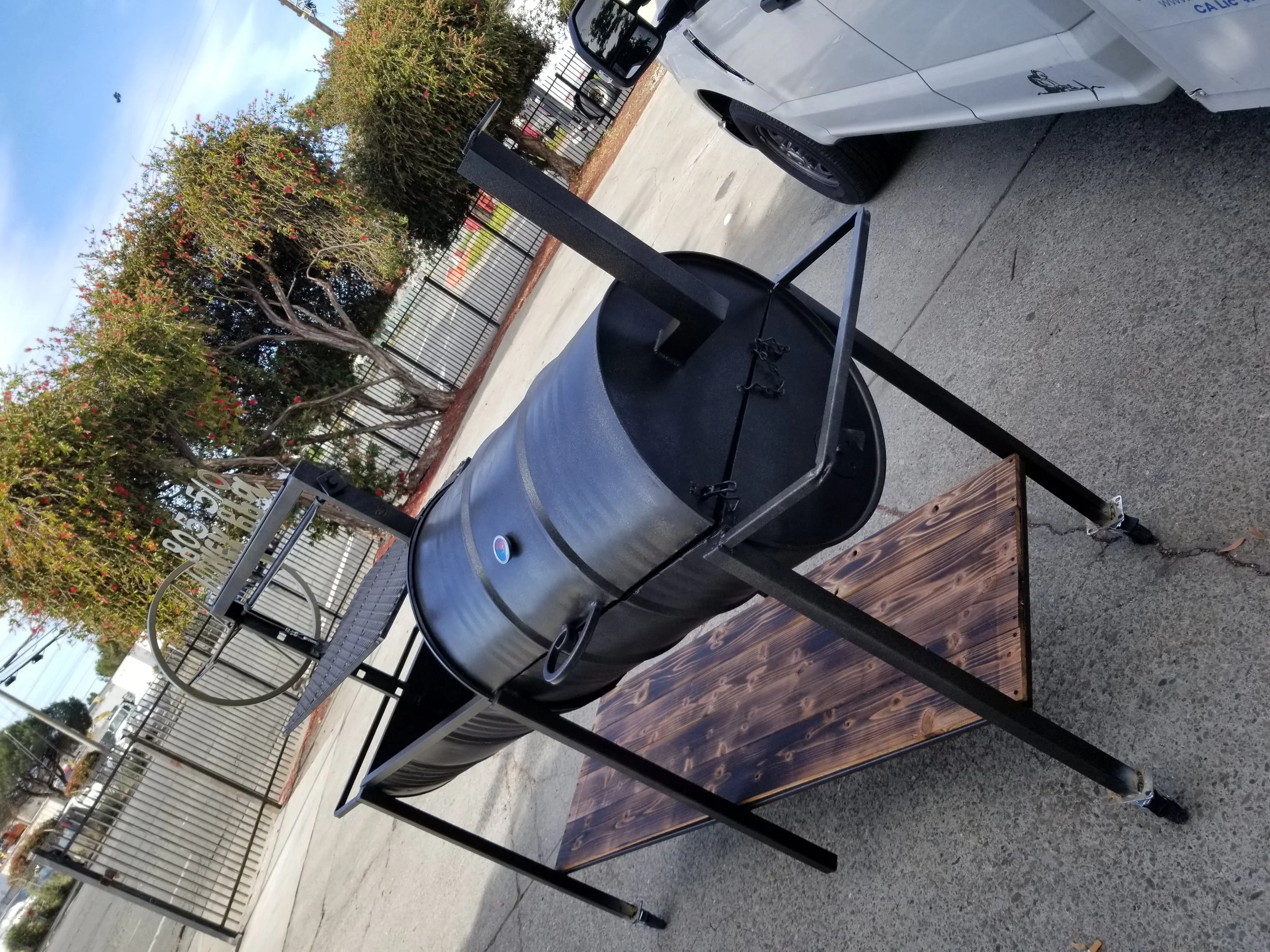 The black bbq pit with the grills made in iron by the professional welder and a wooden base, with the lids closed to protect the grills where they are going to be cooked with cylindrical shape. 